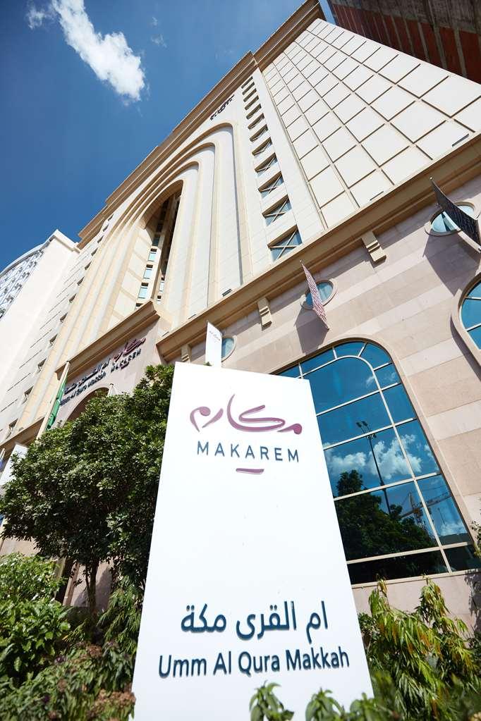 Makarem Umm Al Qura Hotel Mecca Exterior foto The photo shows the exterior of a building featuring a prominent sign that reads "MAKAREM." The design of the building is modern, with large windows and a mix of light-colored stone and other materials. There are decorative elements and flags on the 