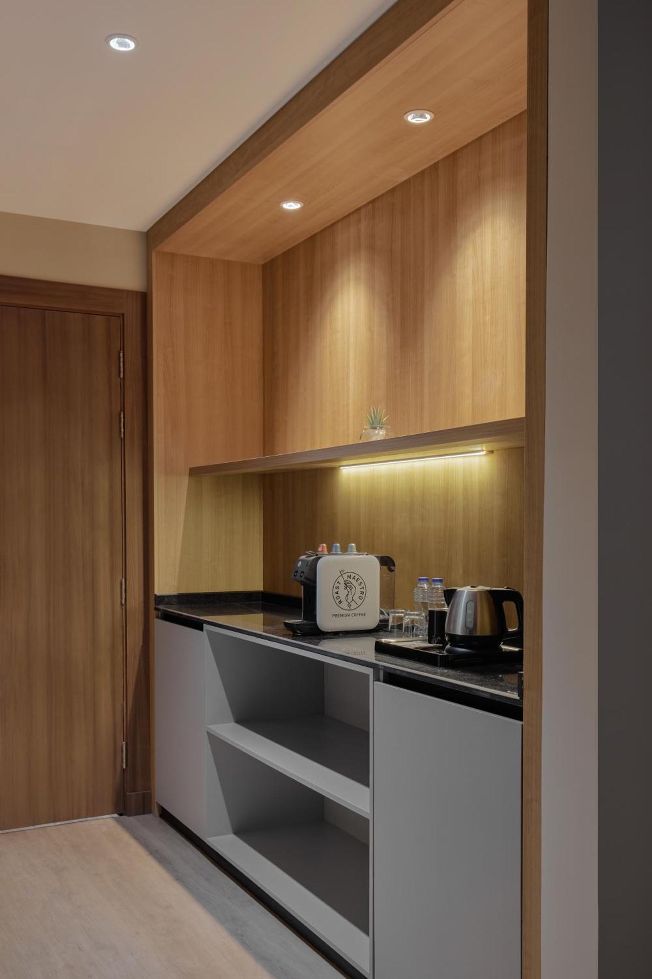 Makarem Umm Al Qura Hotel Mecca Exterior foto The photo shows a small kitchenette area with wooden cabinetry. The upper cabinets feature a light wood finish, while there is a black countertop below. On the countertop, there is a coffee machine, a kettle, and a few glassware items. Soft lighting 