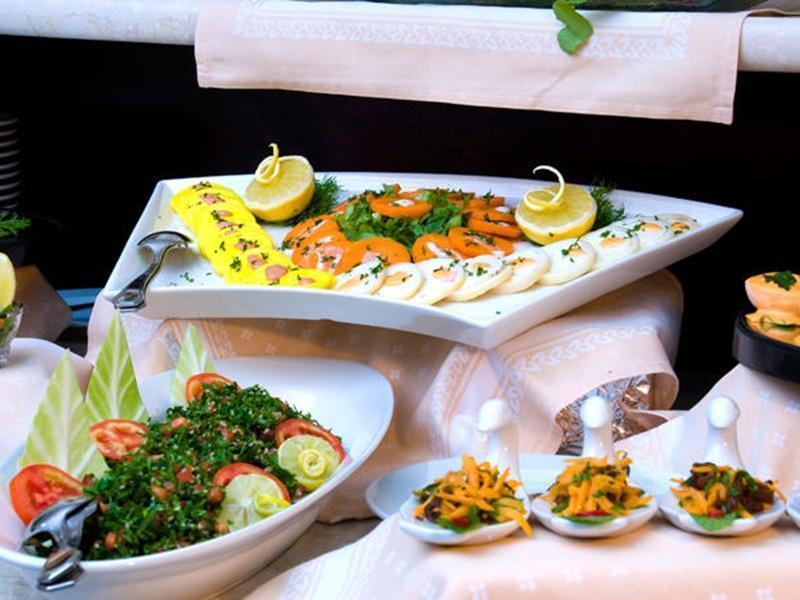 Makarem Umm Al Qura Hotel Mecca Exterior foto The photo displays an assortment of food laid out on a table. In the center, there is a large platter featuring various sliced items, garnished with herbs and lemon wedges. The platter includes colorful ingredients, likely a mix of vegetables and pos