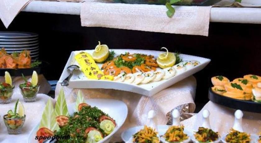 Makarem Umm Al Qura Hotel Mecca Exterior foto The photo shows a beautifully arranged platter of food. On a triangular white plate, there are neatly arranged slices of smoked salmon, garnished with lemon slices and some herbs. Surrounding the salmon are other items that appear to be slices of a l