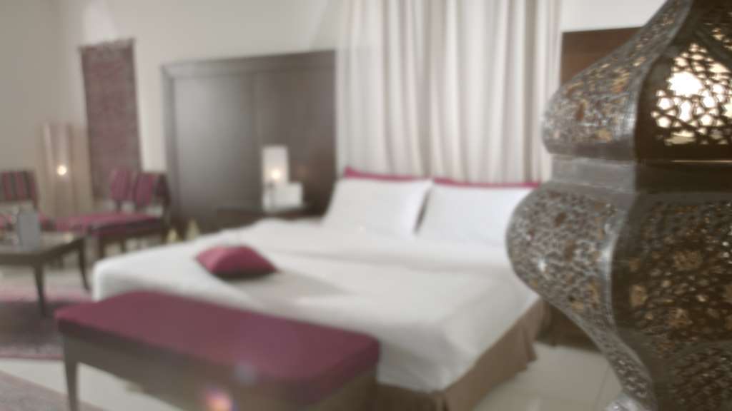 Makarem Umm Al Qura Hotel Mecca Cameră foto The image depicts a bedroom with a modern and elegant design. In the foreground, there is a large, neatly made bed with white linens and a purple decorative pillow. To the side, there is a long bench in a matching purple color. The background feature