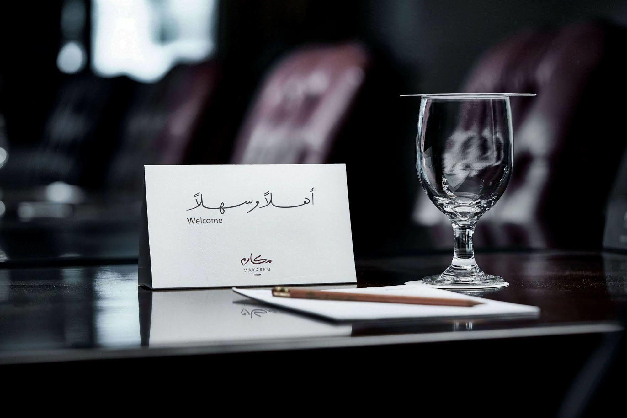 Makarem Umm Al Qura Hotel Mecca Exterior foto The photo depicts a refined setup on a polished table. There is a small welcome card, which includes the word "Welcome" written in English, alongside Arabic script. Also present is a clear glass, presumably for drinking, and a wooden pencil resting o
