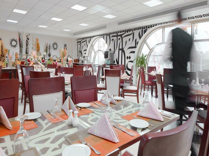 Makarem Umm Al Qura Hotel Mecca Exterior foto The photo shows an interior of a restaurant featuring a modern and elegant design. The dining area includes tables set with white plates, folded napkins, and glassware. The furniture consists of brown and white chairs arranged around the tables. A la