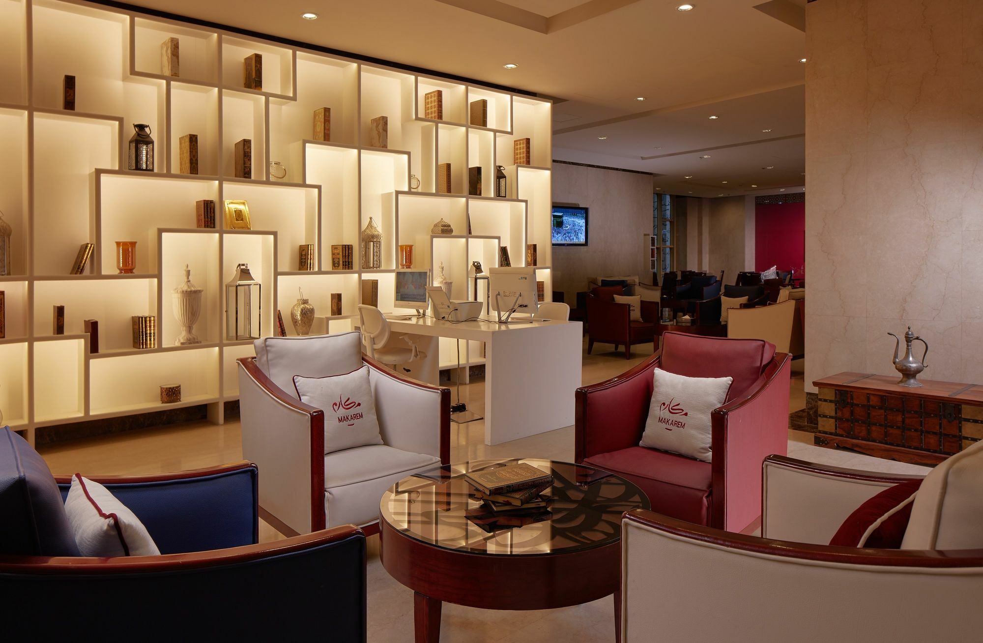 Makarem Umm Al Qura Hotel Mecca Exterior foto The photo depicts a modern and stylish interior space, likely a lounge or seating area. There are comfortably arranged chairs in various colors, including white, red, and blue, surrounding a circular glass-topped table. Behind the seating area, there