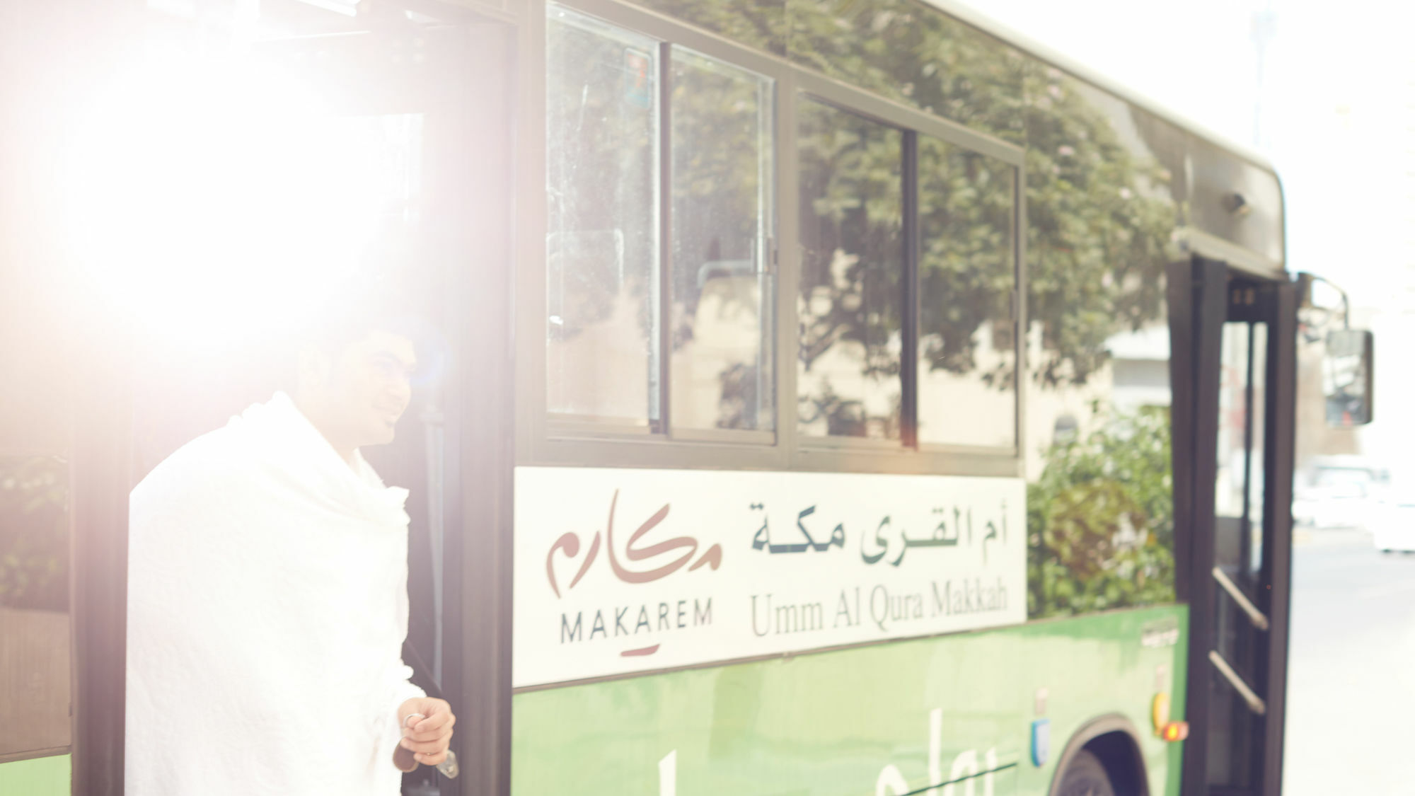 Makarem Umm Al Qura Hotel Mecca Exterior foto The photo features a bus labeled "Makarim" with Arabic text, indicating it operates in the area of Umm Al Qura Makkah. A person dressed in traditional attire is seen stepping out of the bus. The sunlight creates a bright effect, adding a warm ambianc